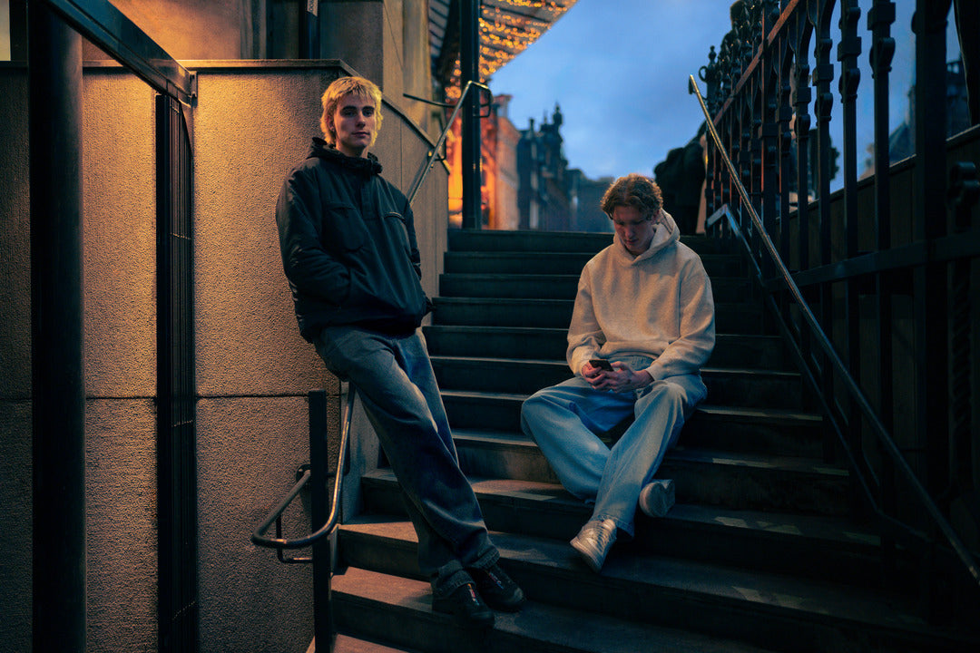 Modellen op een trap dragen baggy jeans zwart en baggy jeans blauw voor lange mannen.