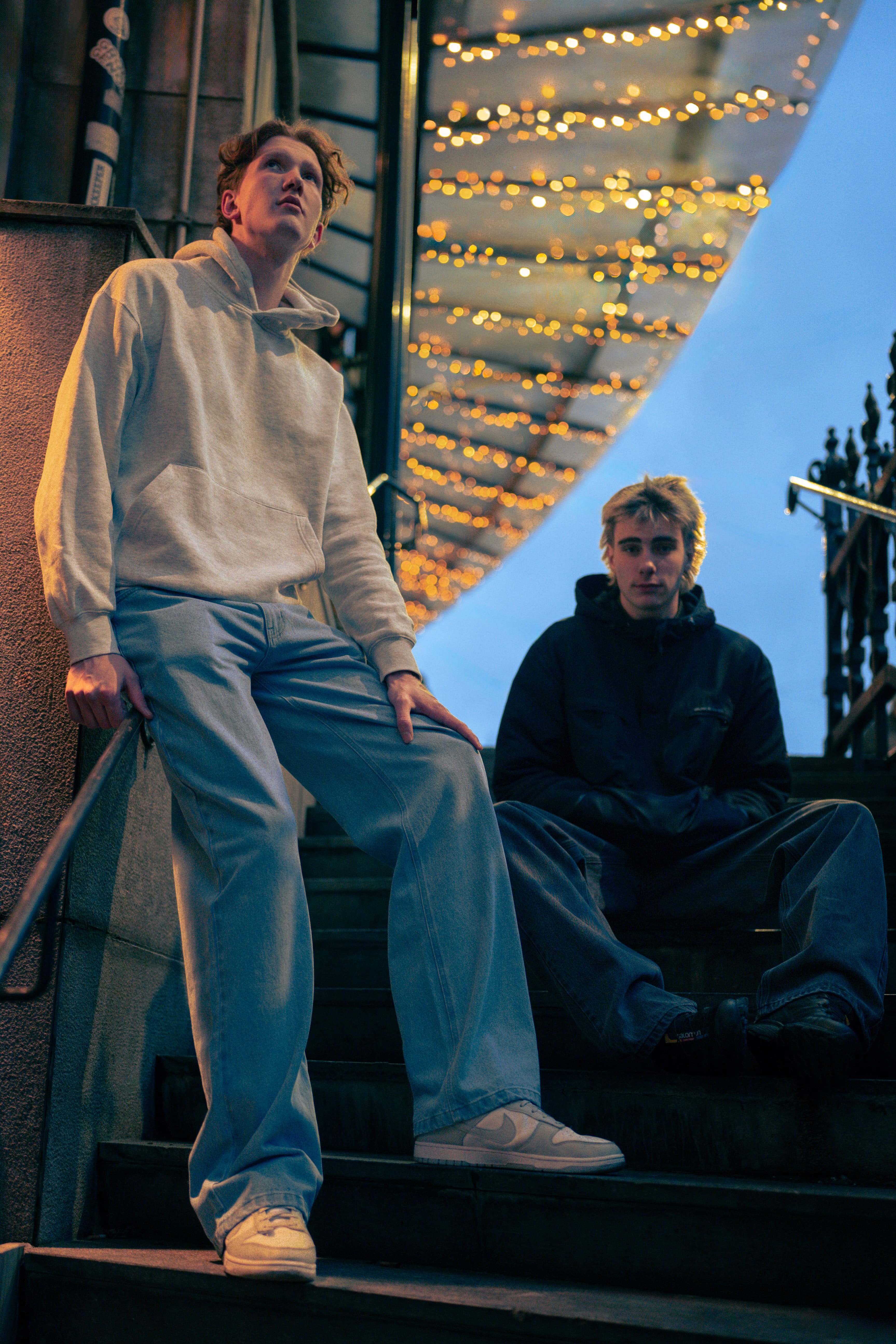 Modellen op een trap, één draagt baggy jeans blauw voor lange mannen en de ander baggy jeans zwart voor lange mannen.